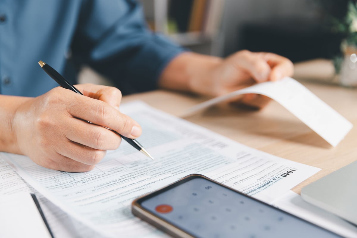 Persona física firmando su declaración anual de impuestos con calculadora y recibos en el escritorio